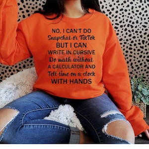 Può includere: Felpa arancione con una stampa grafica nera che dice "NO, I CAN'T DO Snapchat or Tik Tok BUT I CAN WRITE IN CURSIVE Do math without A CALCULATOR AND Tell time on a clock WITH HANDS".