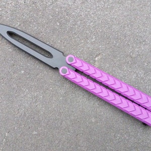 Puede incluir: Un cuchillo mariposa morado con una hoja negra. El mango tiene un patr&oacute;n texturizado.