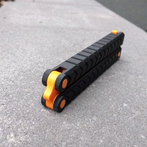Puede incluir: Un cuchillo plegable de bolsillo negro con detalles naranjas. El cuchillo tiene un mango texturizado y est&aacute; cerrado.