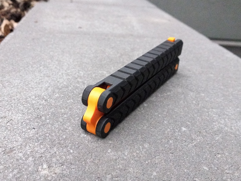 Puede incluir: Un cuchillo plegable de bolsillo negro con detalles naranjas. El cuchillo tiene un mango texturizado y est&aacute; cerrado.