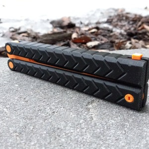 Puede incluir: Un cuchillo plegable de bolsillo negro y naranja con un mango texturizado. El cuchillo est&aacute; cerrado y tiene un seguro de seguridad.