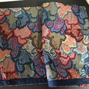 May include: Two patterned fabric panels with a repeating design in shades of blue, red, orange, and brown. The pattern features organic shapes and floral elements. A dark blue border trims the bottom edge of each panel.