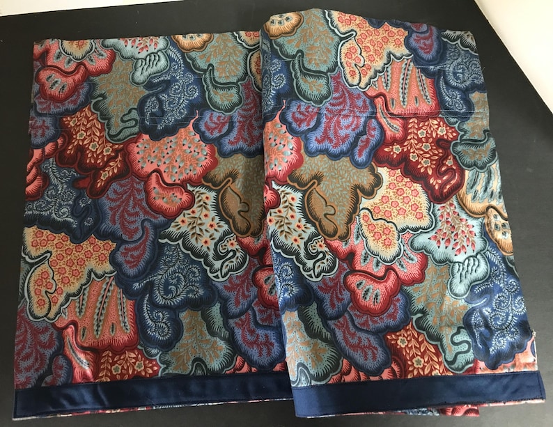 May include: Two patterned fabric panels with a repeating design in shades of blue, red, orange, and brown. The pattern features organic shapes and floral elements. A dark blue border trims the bottom edge of each panel.
