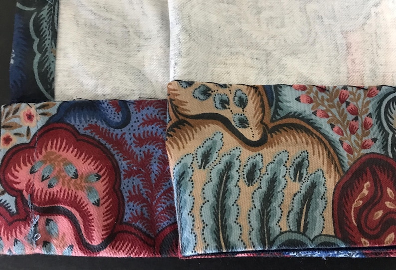May include: Close-up of fabric samples with intricate floral and paisley patterns in shades of red, blue, tan, and pink. The fabric has a vintage aesthetic, with a detailed design and a soft texture.