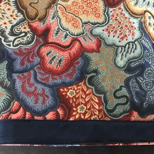 May include: Close-up of two fabric panels with a floral pattern in shades of red, blue, brown, and peach. The bottom edge of each panel has a dark blue border. The fabric has a detailed, ornate design.