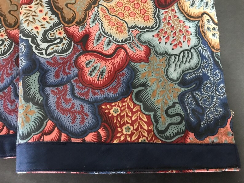 May include: Close-up of two fabric panels with a floral pattern in shades of red, blue, brown, and peach. The bottom edge of each panel has a dark blue border. The fabric has a detailed, ornate design.