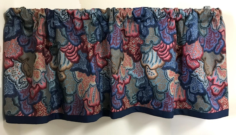 May include: A valance with a repeating pattern of abstract shapes in shades of blue, red, and gray. The fabric is gathered at the top and has a dark blue border along the bottom edge. This decorative valance is designed for a window.