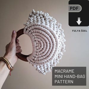 Op de afbeelding: Een wit macramé mini handtaspatroon met een houten handvat. Het patroon is beschikbaar als PDF-download. De tekst op de afbeelding luidt "MACRAME MINI HAND-BAG PATTERN FULYA ÖZEL"