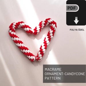 Puede incluir: Un adorno de macramé en forma de corazón rojo y blanco, con un icono de descarga PDF y el texto "FULYA ÖZEL" debajo. El texto "MACRAME ORNAMENT-CANDYCONE PATTERN" está en la parte inferior de la imagen.