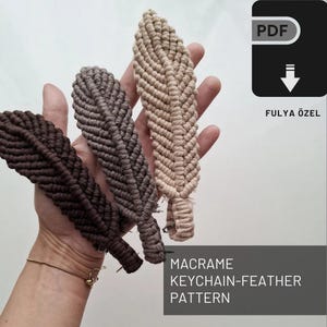 Może przedstawiać: Trzy breloki z frędzlami w kształcie pióra w kolorze brązowym, szarym i beżowym. Breloki wiszą na dłoni. Obraz zawiera tekst "MACRAME KEYCHAIN-FEATHER PATTERN" i "FULYA ÖZEL".