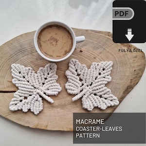Puede incluir: Dos posavasos de macramé en forma de hoja beige sobre una superficie de madera con una taza de café. El texto "MACRAME COASTER-LEAVES PATTERN" está debajo de los posavasos.