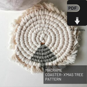 Könnte beinhalten: Ein weißer und grauer Makramee-Untersetzer mit Fransenrand. Der Untersetzer ist in Form eines Weihnachtsbaums gestaltet. Der Text "MACRAME COASTER-X'MAS TREE PATTERN" ist unter dem Untersetzer gedruckt.