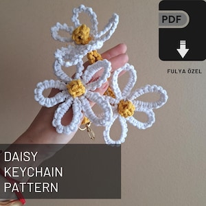May include: A crochet pattern for a daisy keychain. The pattern includes instructions for making a white daisy with a yellow center. The pattern is available as a PDF download.  "FULYA ÖZEL" is printed on the PDF download button.