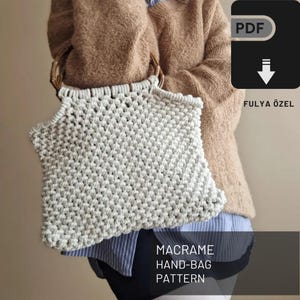Könnte beinhalten: Eine weiße Makramee-Handtasche mit Holzgriffen. Die Tasche wird von einer Person gehalten, die einen braunen Pullover trägt. Der Text "MACRAME HAND-BAG PATTERN" befindet sich am unteren Rand des Bildes. Der Text "FULYA ÖZEL" befindet sich unten rechts im Bild.