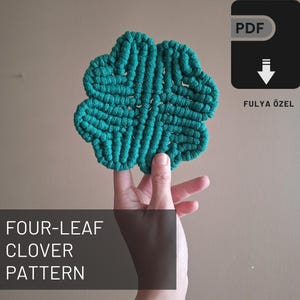 May include: A green four-leaf clover macrame pattern, made with string, is held in a hand. The pattern is available as a PDF download. The text "FOUR-LEAF CLOVER PATTERN" is at the bottom of the image.