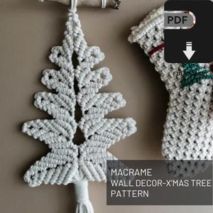 May include: A white macrame Christmas tree wall decor pattern. The tree is made of knotted rope and is hanging from a wooden branch. The image also includes a partial view of another macrame decoration. Text on the image reads "MACRAME WALL DECOR-X'MAS TREE PATTERN".