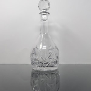 May include: A clear glass decanter with a faceted stopper. The decanter has a starburst pattern etched into the glass.
