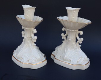May include: A pair of white porcelain candle holders with gold trim. The holders feature a floral design and are in the shape of a traditional candlestick.