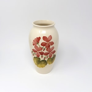 Può includere: Un vaso in ceramica bianca con un disegno floreale. Il vaso presenta fiori rosa e foglie verdi.