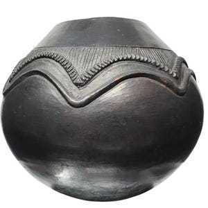 Könnte beinhalten: Ein handgefertigtes, rundes Töpfergefäß in Dunkelgrau mit einem strukturierten, geschnitzten Design am oberen Rand. Das Gefäß hat einen glatten, abgerundeten Körper und einen leicht ausgestellten Rand. Das geschnitzte Design zeigt eine Reihe von wellenförmigen Linien und geometrischen Mustern.