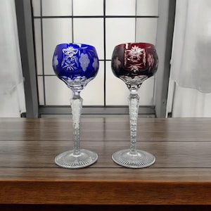 May include: Two stemmed wine glasses with intricate cut glass designs. One glass is blue and the other is red.