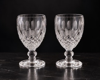 May include: Two clear crystal glasses featuring a detailed diamond-cut pattern on the lower bowl, vertical fluting near the rim, and a thick, rounded stem leading to a circular base. The glasses are transparent with reflective surfaces.