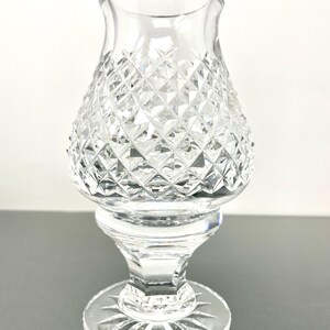 May include: A clear glass candle holder with a diamond-cut pattern on the body. The base is round with a starburst design. The candle holder has a flared top and a pedestal base.