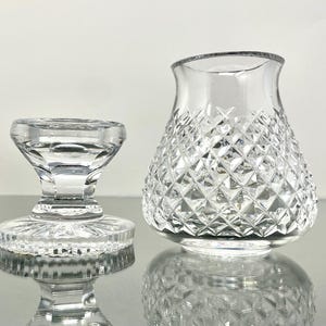 May include: Two clear glass objects. On the left is a small, pedestal-style object with a round base and a flared top. On the right is a vase with a diamond-cut pattern. Both objects are reflecting on a shiny surface.