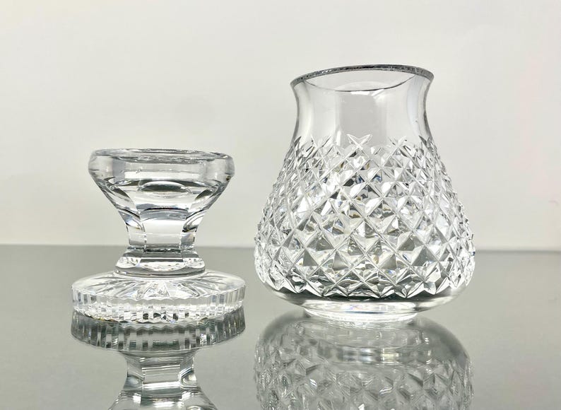May include: Two clear glass objects. On the left is a small, pedestal-style object with a round base and a flared top. On the right is a vase with a diamond-cut pattern. Both objects are reflecting on a shiny surface.