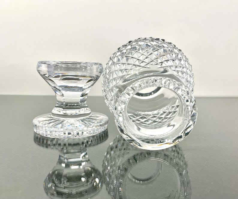 May include: Two clear, cut-glass items. One is a small, round, diamond-patterned glass with a wide opening. The other is a small, pedestal-style glass with a flat, round base and a flared top. Both items are highly reflective.