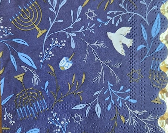 May include: Blue paper napkins with a white and gold design featuring a menorah, a dreidel, a Star of David, and a dove. The napkins have a scalloped edge.