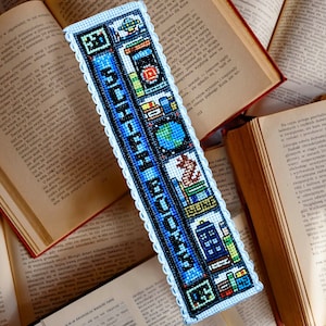 May include: A blue and white cross-stitch bookmark featuring the text "I love to read" and various book-themed images, including a globe, a TARDIS, and a book with a cat on it.