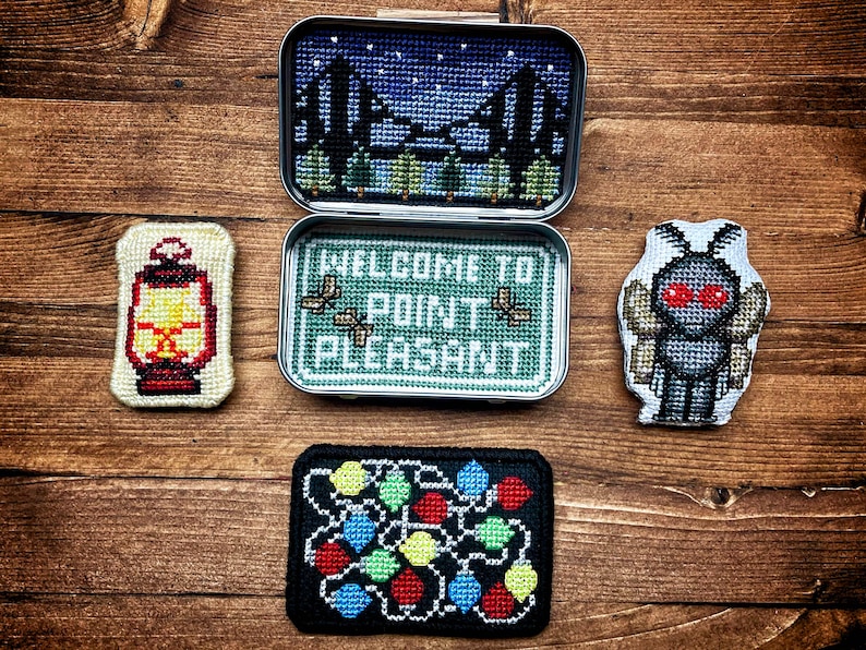 Op de afbeelding: Vier geborduurde patches met een lantaarn, een mot, een lichtsnoer en een blik met de tekst "Welkom in Point Pleasant".