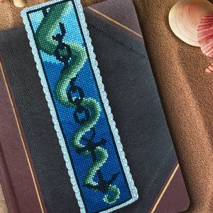 May include: A blue and green embroidered bookmark with a seahorse and anchor design. The bookmark has a white crocheted border.