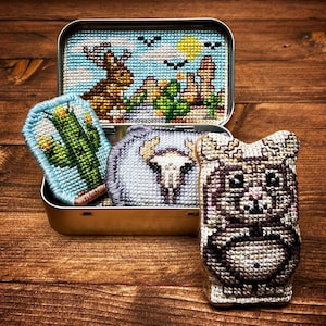 May include: A set of four embroidered patches featuring a cactus, a skull, a deer, and a cartoon animal. The patches are in a small tin box.