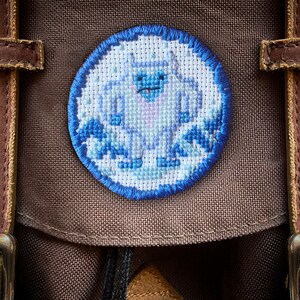 May include: A brown canvas backpack with a blue and white embroidered patch of a yeti in a snowy scene.