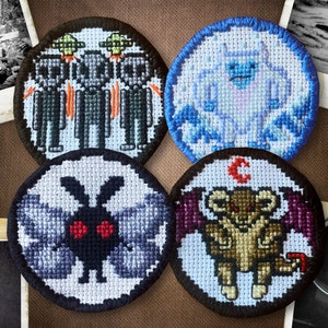 May include: Four embroidered patches featuring different mythical creatures. The patches are circular and have a black border. The first patch features three grey aliens with red eyes and flying saucers. The second patch features a white yeti with blue eyes and a blue background. The third patch features a black moth with red eyes and grey wings. The fourth patch features a brown creature with red eyes and purple wings.