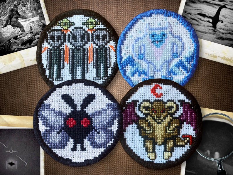 May include: Four embroidered patches featuring different mythical creatures. The patches are circular and have a black border. The first patch features three gray aliens with red eyes and flying saucers. The second patch features a white yeti with blue eyes and a blue background. The third patch features a black moth with red eyes and gray wings. The fourth patch features a brown creature with red eyes and purple wings.