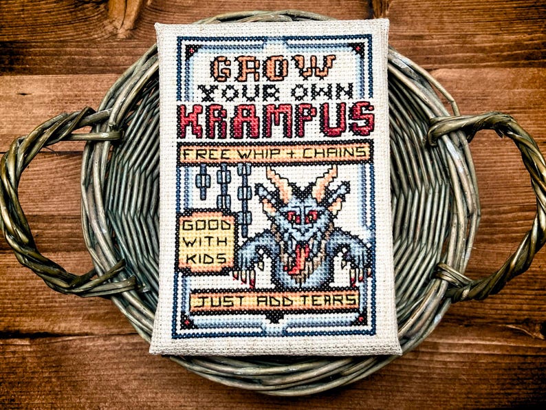 May include: Cross-stitch art piece with the text "GROW YOUR OWN KRAMPUS" and a pixelated Krampus illustration. The design includes the phrases "FREE WHIP + CHAINS", "GOOD WITH KIDS", and "JUST ADD TEARS". The artwork is set in a woven basket.