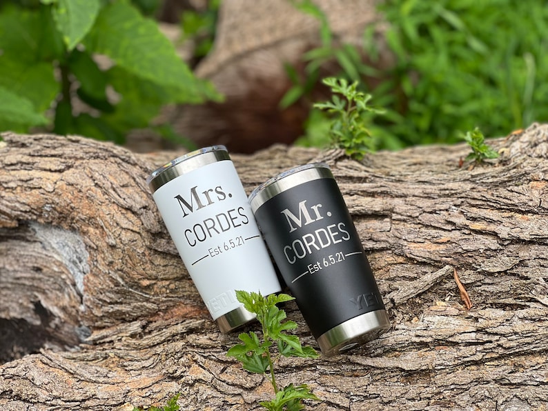 May include: Two stainless steel tumblers with black and white lids. The white tumbler has "Mrs. CORDES - Est 6.5.21" engraved on it. The black tumbler has "Mr. CORDES - Est 6.5.21" engraved on it.