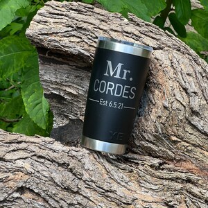 May include: Black stainless steel tumbler with a black lid and a silver inscription that reads "Mr. Cordes - Est 6.5.21".