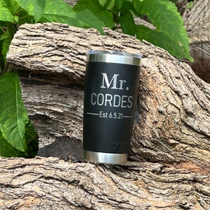 May include: Black stainless steel tumbler with a silver lid. The tumbler has the text "Mr. CORDES - Est 6.5.21" engraved on the side.