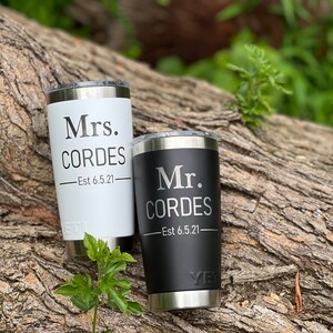 May include: Two personalized stainless steel tumblers, one black and one white, with the text "Mr. Cordes - Est 6.5.21" and "Mrs. Cordes - Est 6.5.21" on them.