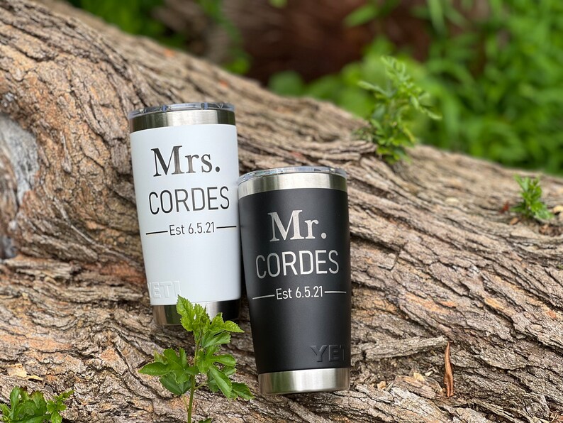 May include: Two personalized stainless steel tumblers, one black and one white, with the text "Mr. Cordes - Est 6.5.21" and "Mrs. Cordes - Est 6.5.21" on them.
