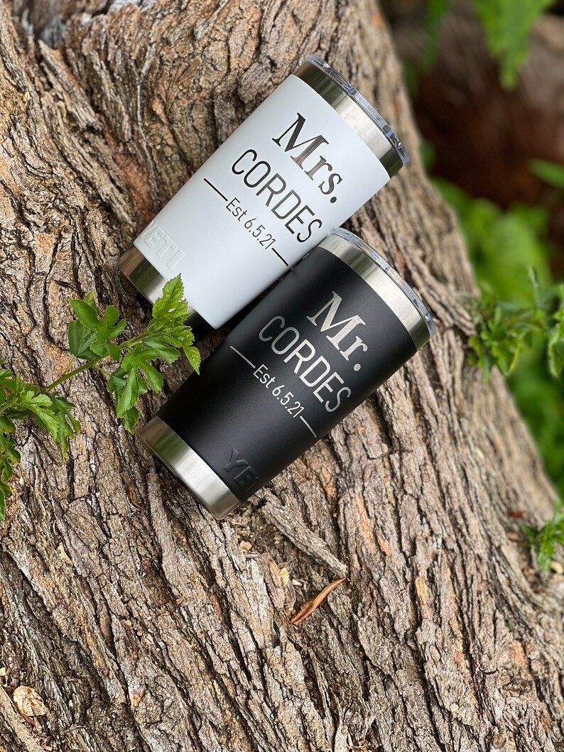 May include: Two stainless steel tumblers with black and white lids. The tumblers are personalized with the text "Mr. Cordes Est 6.5.21" and "Mrs. Cordes Est 6.5.21".