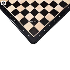 May include: A close-up of a black and beige chessboard. The board features alternating black and beige squares, with a black border. The text "CHESS VILLA" is visible on the board. The board is designed for playing chess.