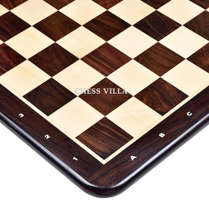 May include: A close-up of a wooden chessboard with alternating dark brown and light beige squares. The board has a dark brown border with white alphanumeric markings. The text "CHESS VILLA" is visible on the board.