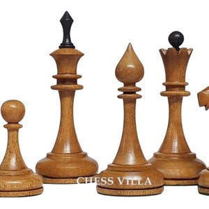 Op de afbeelding: Een set van zes lichtbruine houten schaakstukken, waaronder een toren, pion, koning met een zwarte knop, loper, koningin met een zwarte bolvormige top en een paard. De tekst CHESS VILLA is in het wit gedrukt op de voet van de koning en loper.