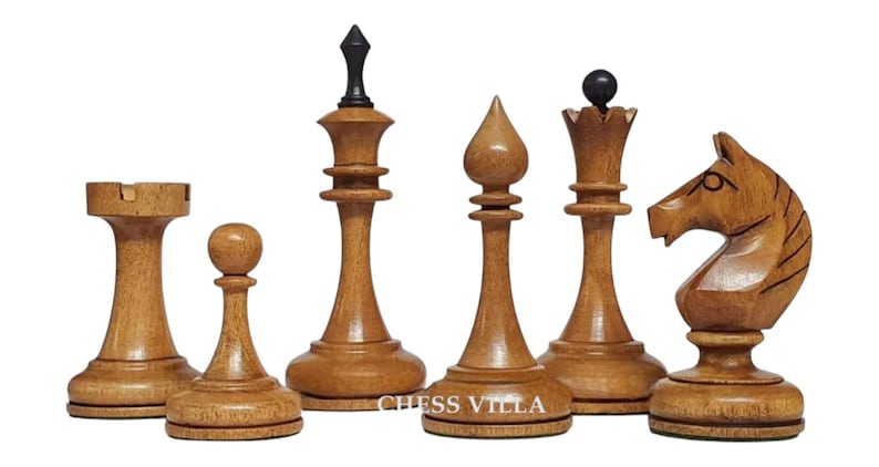 Op de afbeelding: Een set van zes lichtbruine houten schaakstukken, waaronder een toren, pion, koning met een zwarte knop, loper, koningin met een zwarte bolvormige top en een paard. De tekst CHESS VILLA is in het wit gedrukt op de voet van de koning en loper.