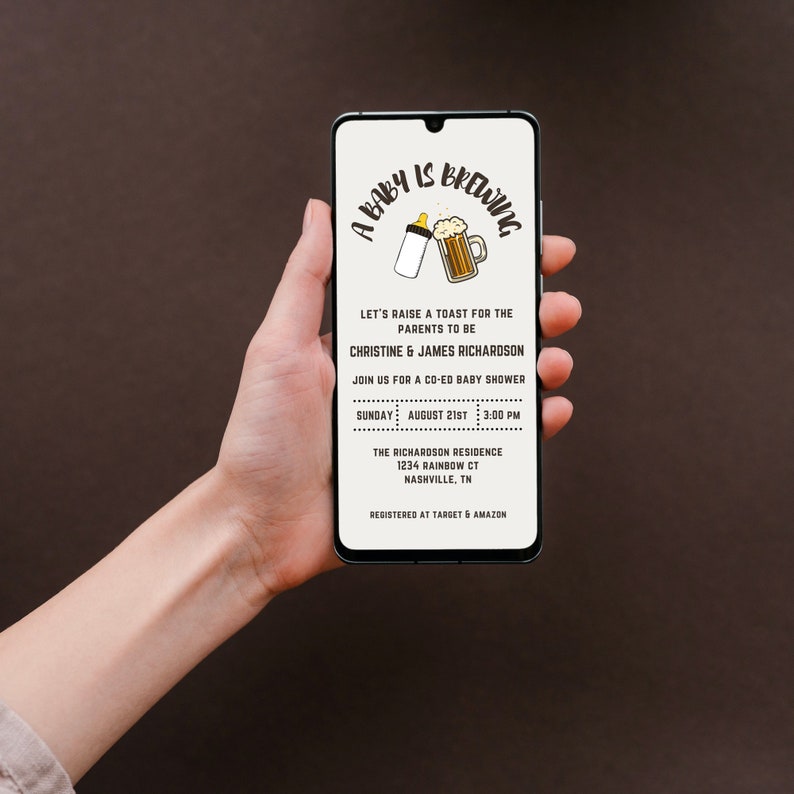 Op de afbeelding: Een smartphone toont een uitnodiging voor een babyshower. De uitnodiging bevat de tekst "A Baby is Brewing" met illustraties van een babyfles en een bierpul. Details zijn de namen van de ouders, datum, tijd en locatie.